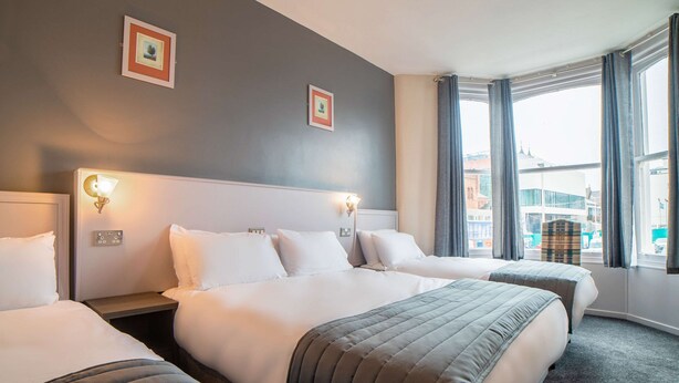 A hotel room with three beds, a large window with curtains, and two wall-mounted light fixtures. - Comfort Inn Blackpool Gresham (Blackpool)