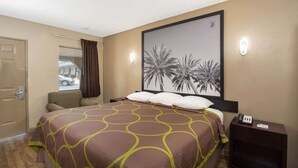 A hotel room with a large bed, a nightstand with a phone, a wall-mounted light, and a window with curtains.