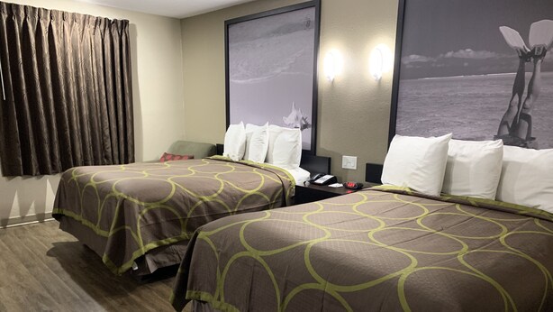 A hotel room with two beds, a desk, a telephone, and a wall with a picture.