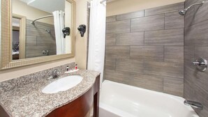 A bathroom with a granite countertop sink, a large mirror, a shower with a curtain, and a bathtub.