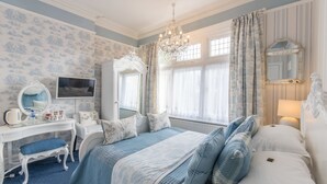 Un dormitorio con una cama, un tocador con espejo, un aparador y una ventana con cortinas.