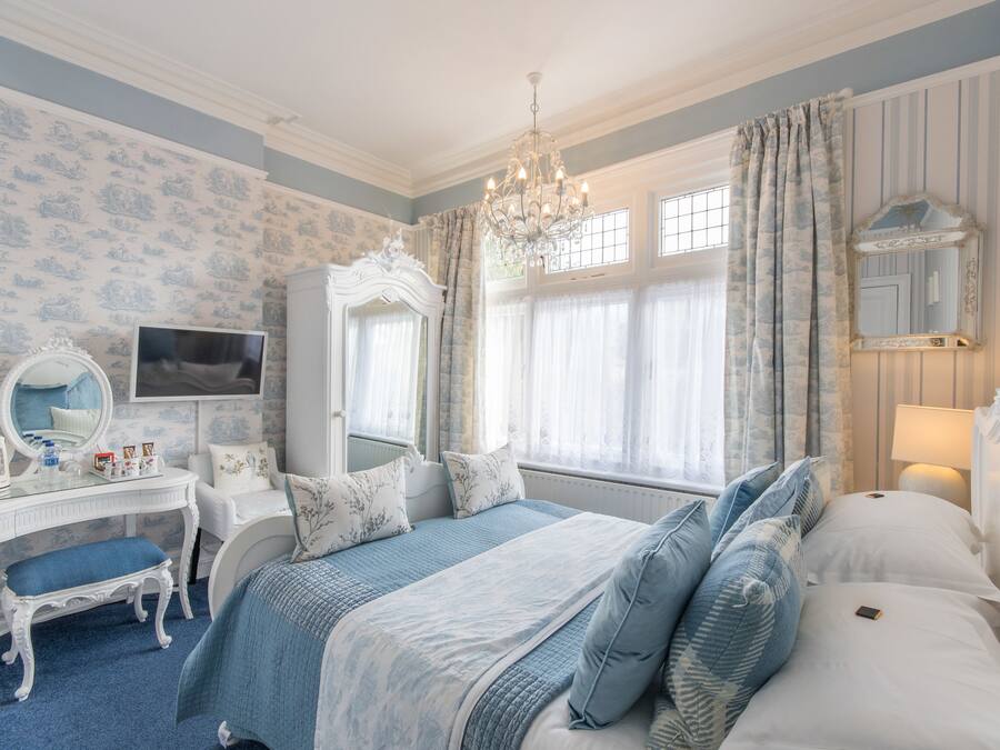 Een slaapkamer met een bed, een kaptafel met spiegel, een dressoir en een raam met gordijnen.