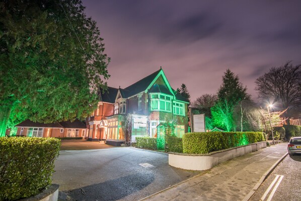 A large, traditional house with a steeply pitched roof and multiple chimneys, surrounded by well-maintained hedges and trees. - Grovefield Manor (Poole)