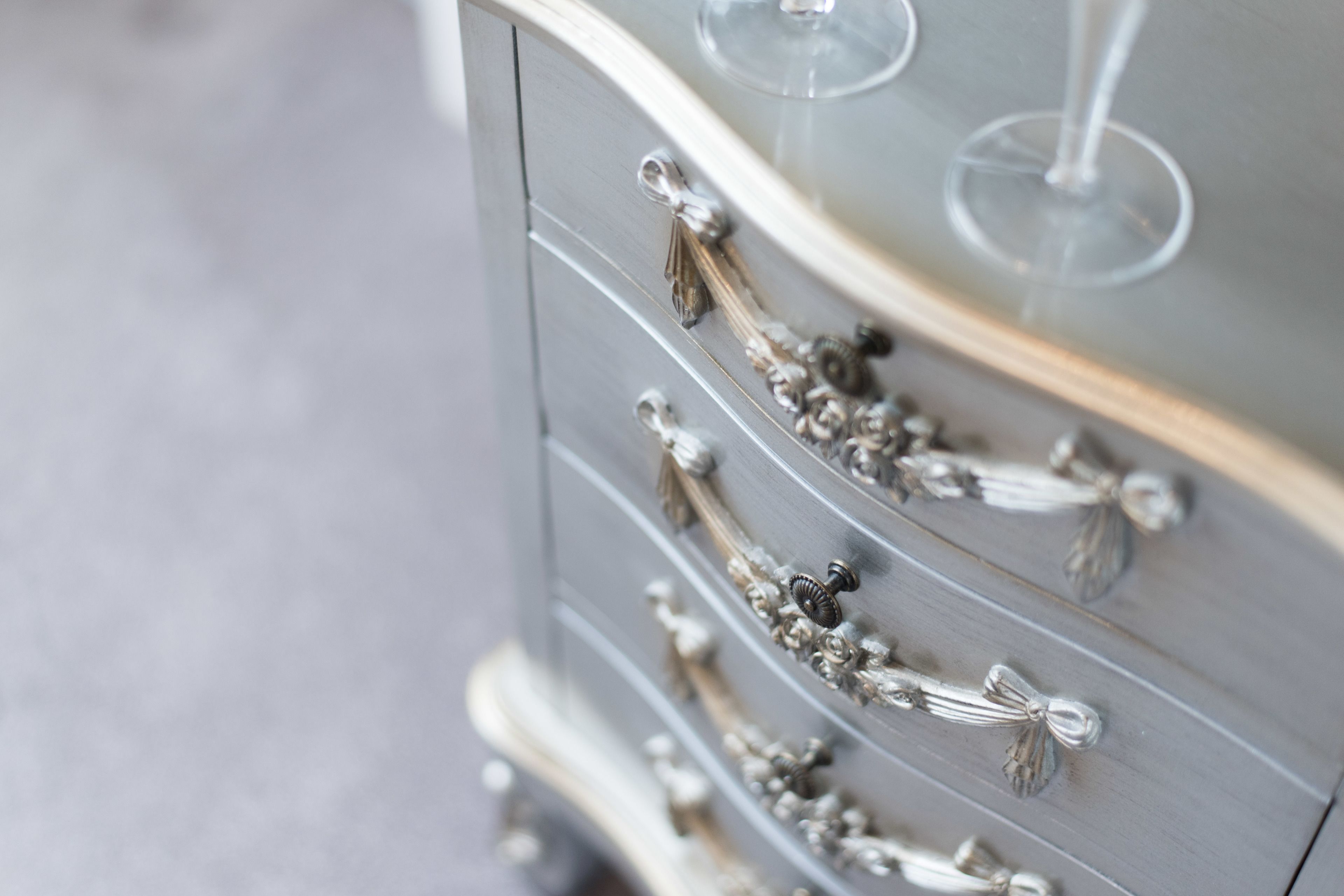 A close-up of a dresser with ornate silver handles and a wine glass on top.
