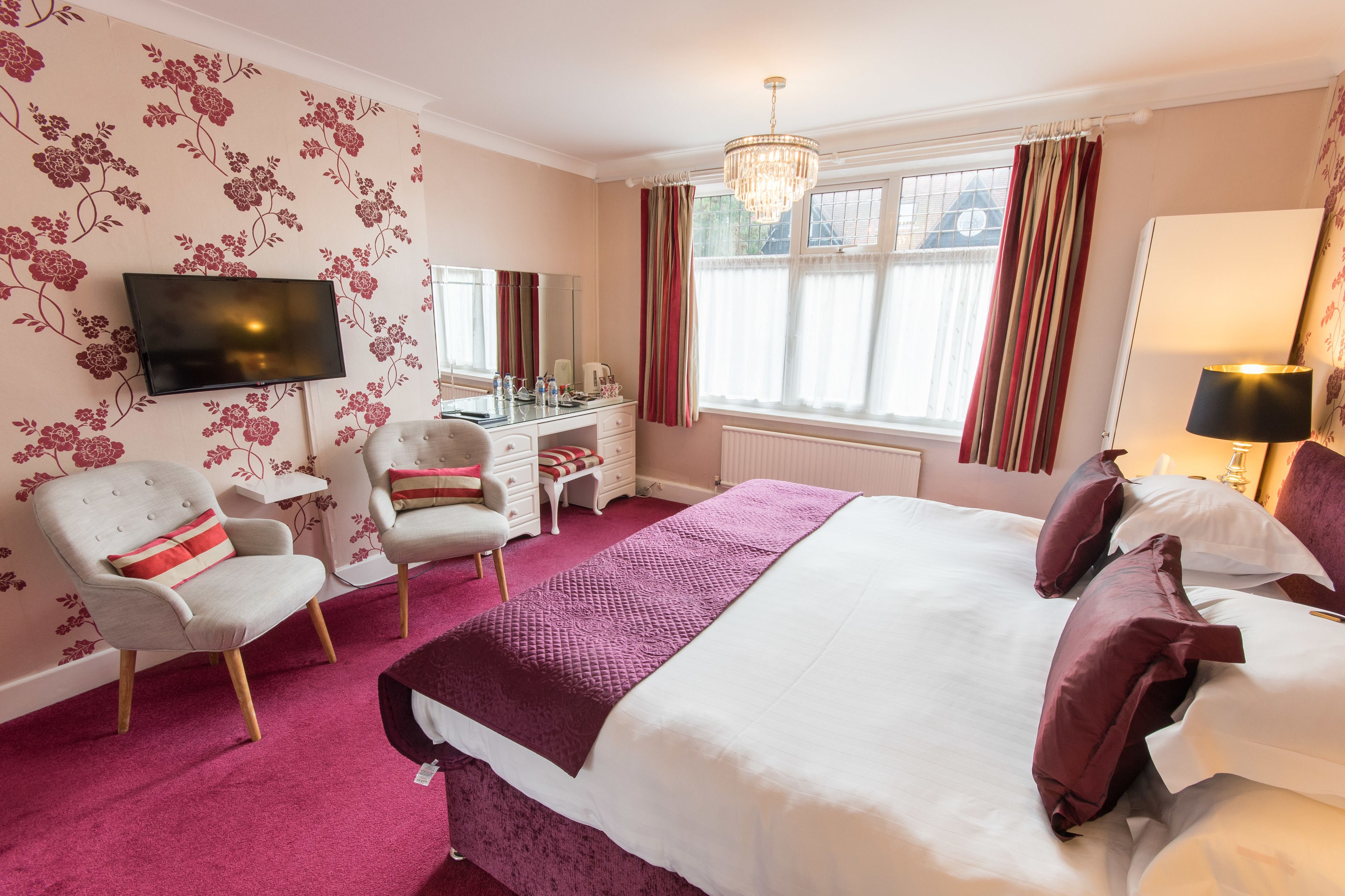 A hotel room with a large bed, a desk, a chair, a television, and a window with curtains.