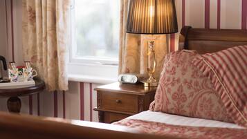 Een slaapkamer met een bed, een nachtkastje met een lamp, een klok en een raam met gordijnen.