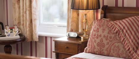 A bedroom with a bed, a bedside table with a lamp, a clock, and a window with curtains.