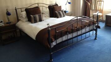 A neatly made bed with a metal frame, a blue carpet, and a bedside table with a lamp.