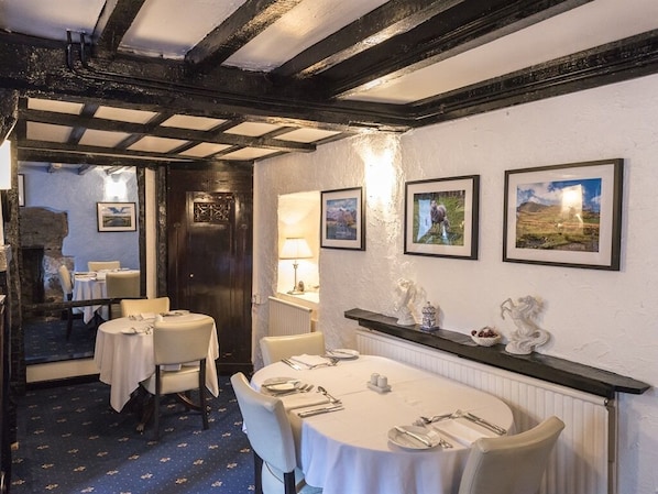 A dining area with round tables set for four, white tablecloths, and a rustic ceiling with exposed beams.