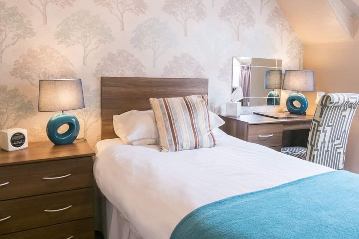 A bedroom with a bed, bedside tables, lamps, a desk, and a chair.