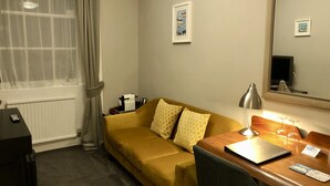 Een hotelkamer met een bank, een bureau met een lamp, een spiegel en een raam met gordijnen.