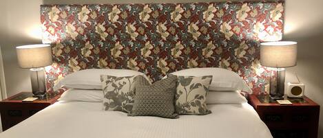 A neatly made bed with floral-patterned headboard, two bedside lamps, and a small radio on the nightstand.