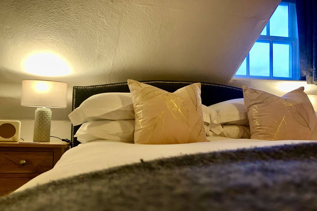 Ein Schlafzimmer mit Bett, Kissen, einer Nachttischlampe und einem Fenster.