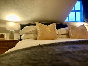 A bedroom with a bed, pillows, a bedside lamp, and a window.