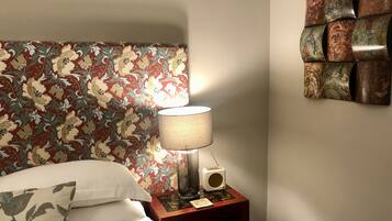 A neatly made bed with floral-patterned headboard, a bedside lamp, a radio, and a decorative wall piece.