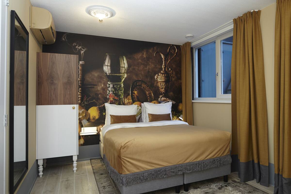A bedroom with a bed, a wardrobe, a nightstand, a mirror, and a window with curtains.