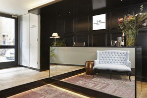 Een receptiegedeelte met een witte bank, een bureau, een lamp en een vaas met bloemen.