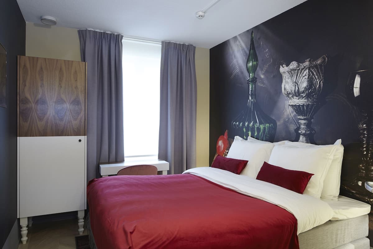 A hotel room with a bed, a desk, and a large wall mural.