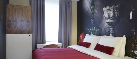 A hotel room with a bed, a desk, and a large wall mural.