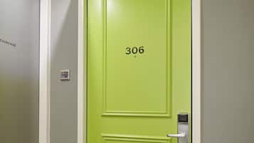 A green door with the number 306, a security camera, and a fire alarm on the wall.