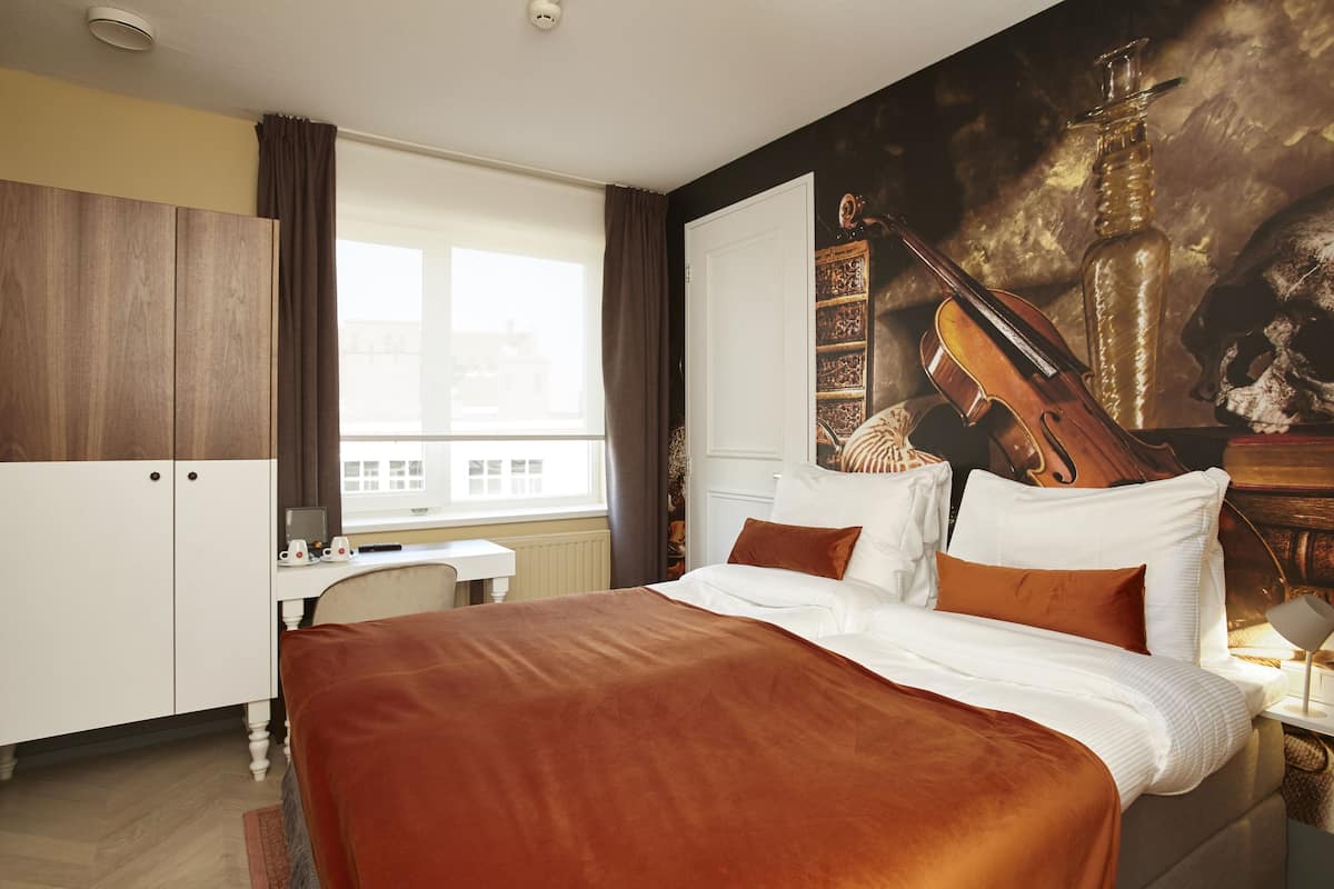A hotel room with a bed, a desk, and a large window.
