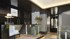 Eine moderne Lobby mit einem weißen Sofa, einer Glastrennwand, einer Treppe und einem Schild für The Muse Amsterdam.
