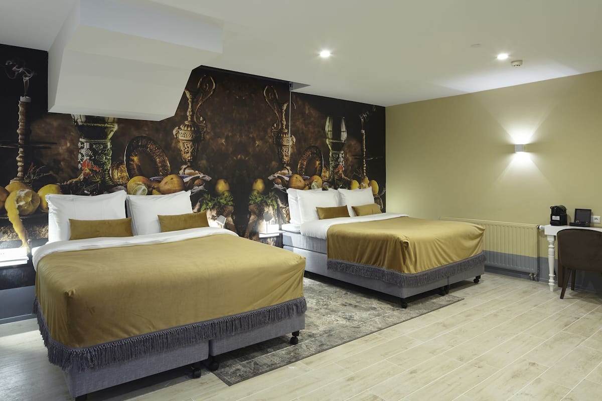 A hotel room with two beds, a large mural, a desk, and a chair.