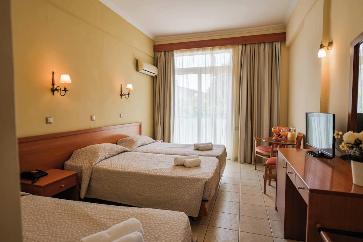 Habitación de hotel con tres camas, un escritorio con televisor y un comedor con mesa y sillas.