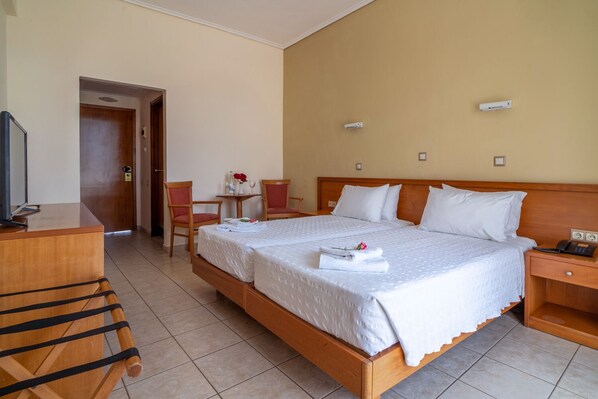 Habitación de hotel con cama doble, escritorio, dos sillas, televisor y una mesita con un florero y copas de vino.