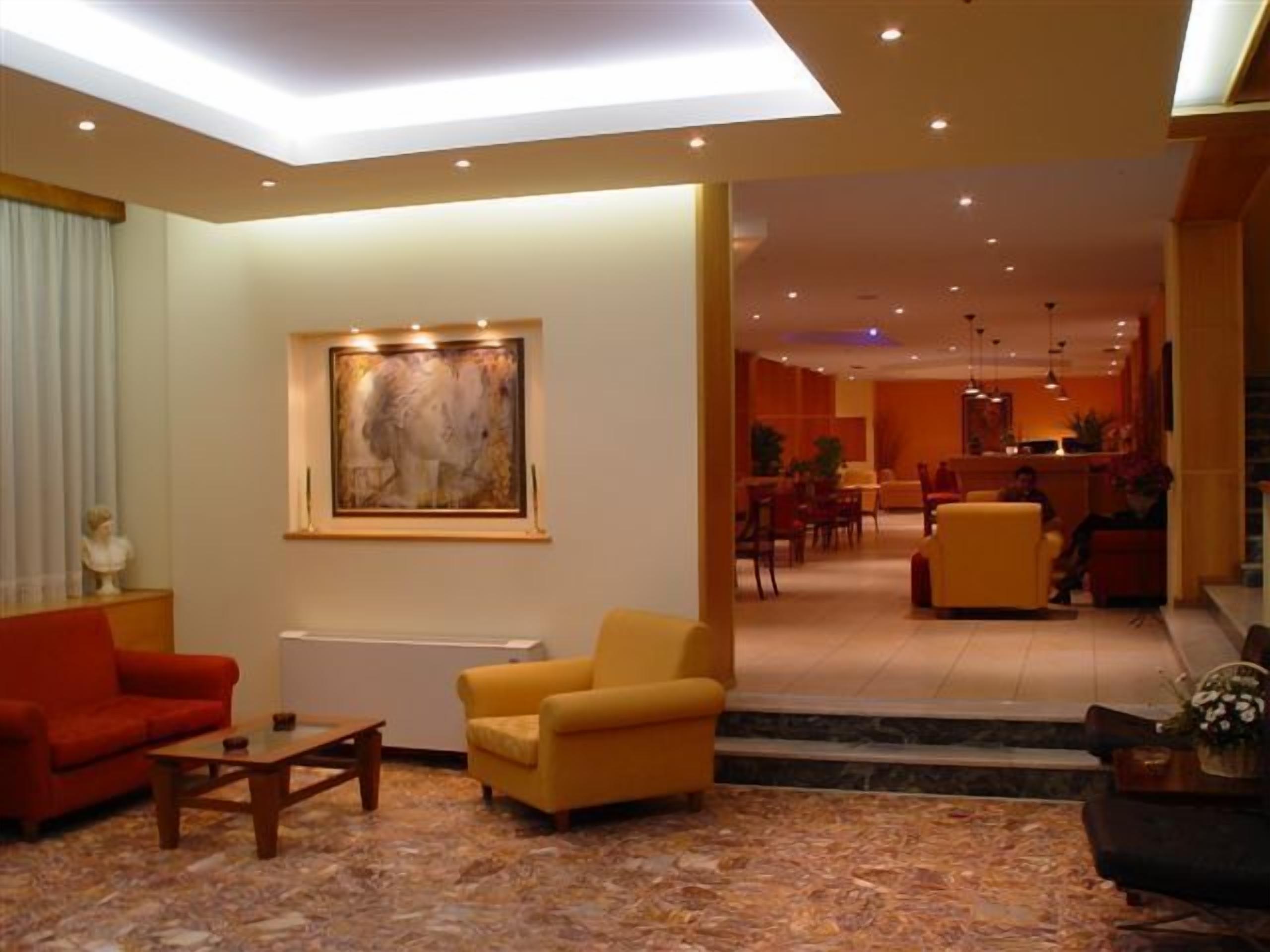 Un hall d’hôtel au design moderne, avec un grand tableau abstrait, un canapé rouge, un fauteuil jaune et, au fond, un espace repas.