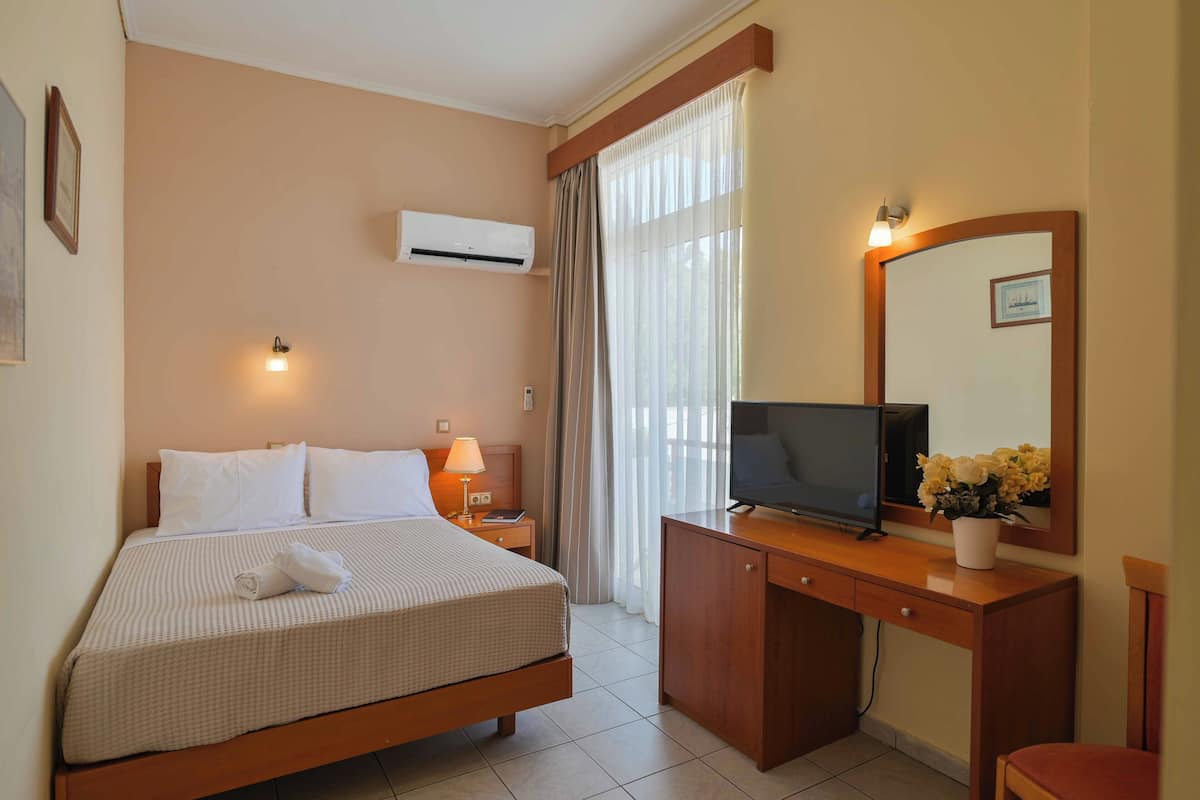 Habitación de hotel con cama, escritorio con televisor, espejo y ventana con cortinas.
