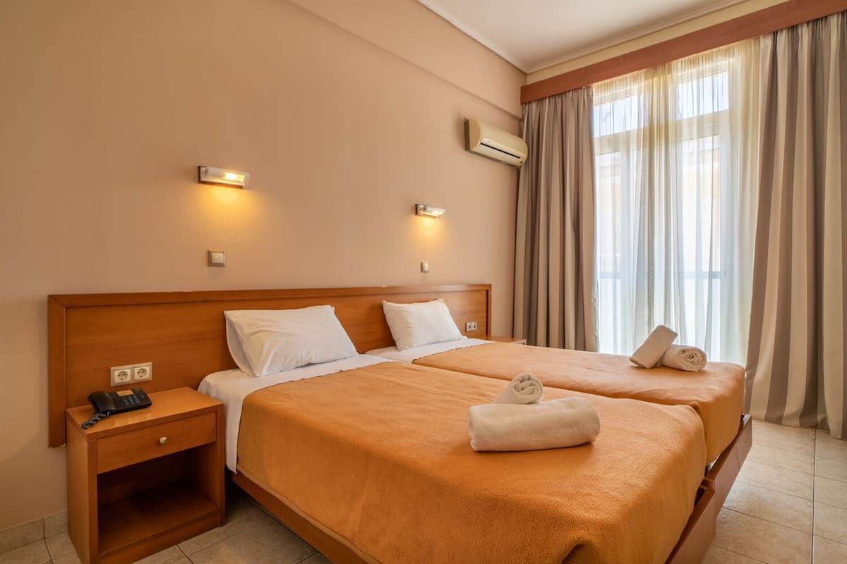 Habitación de hotel con dos camas, una mesita de noche de madera con un teléfono y un aire acondicionado instalado en la pared.