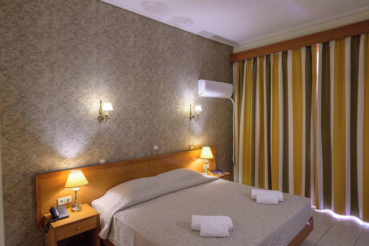 Habitación de hotel con una cama grande, dos lámparas de noche, un teléfono y aire acondicionado instalado en la pared.