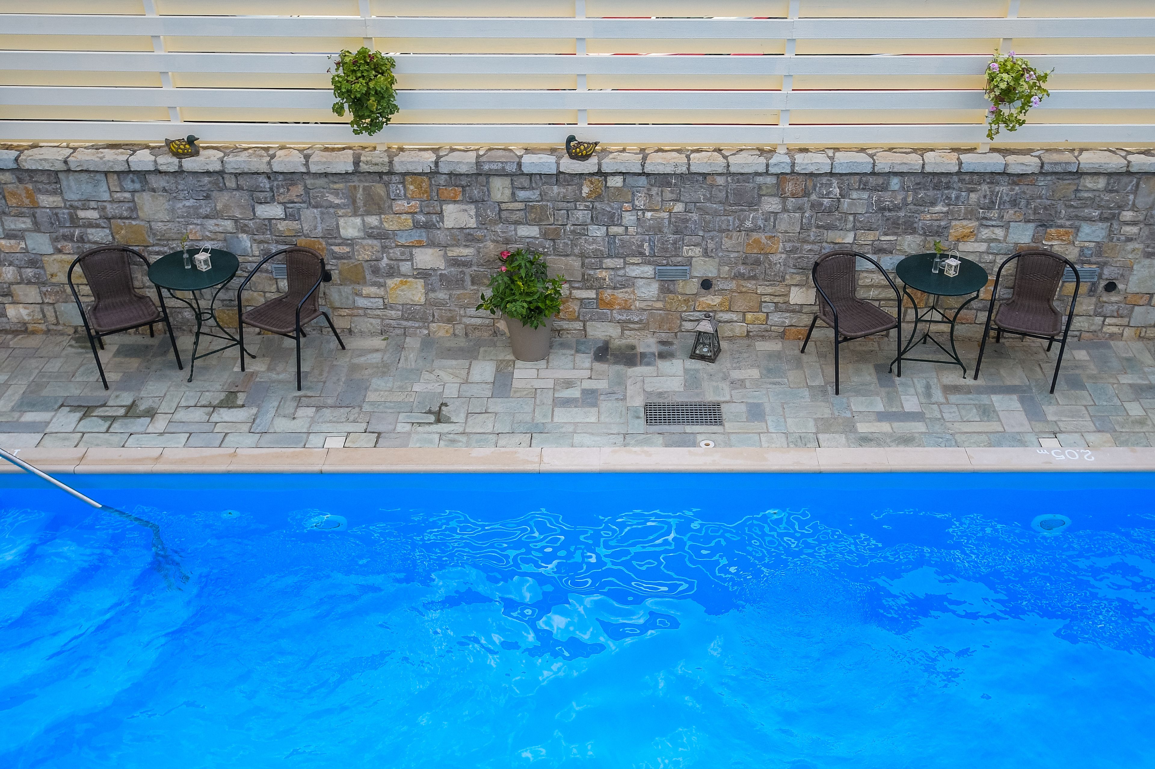 An outdoor pool area with stone walls, wicker chairs, and potted plants.