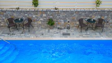 Zona de piscina al aire libre con paredes de piedra, sillas de mimbre y plantas en macetas.