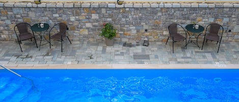 An outdoor pool area with stone walls, wicker chairs, and potted plants.