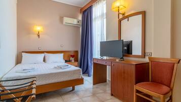 A hotel room with a bed, a desk with a TV, a chair, and a window with curtains.