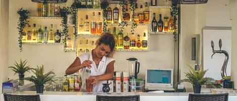 Zona de bar con estantes llenos de botellas de licor, una barra y un monitor de computadora.