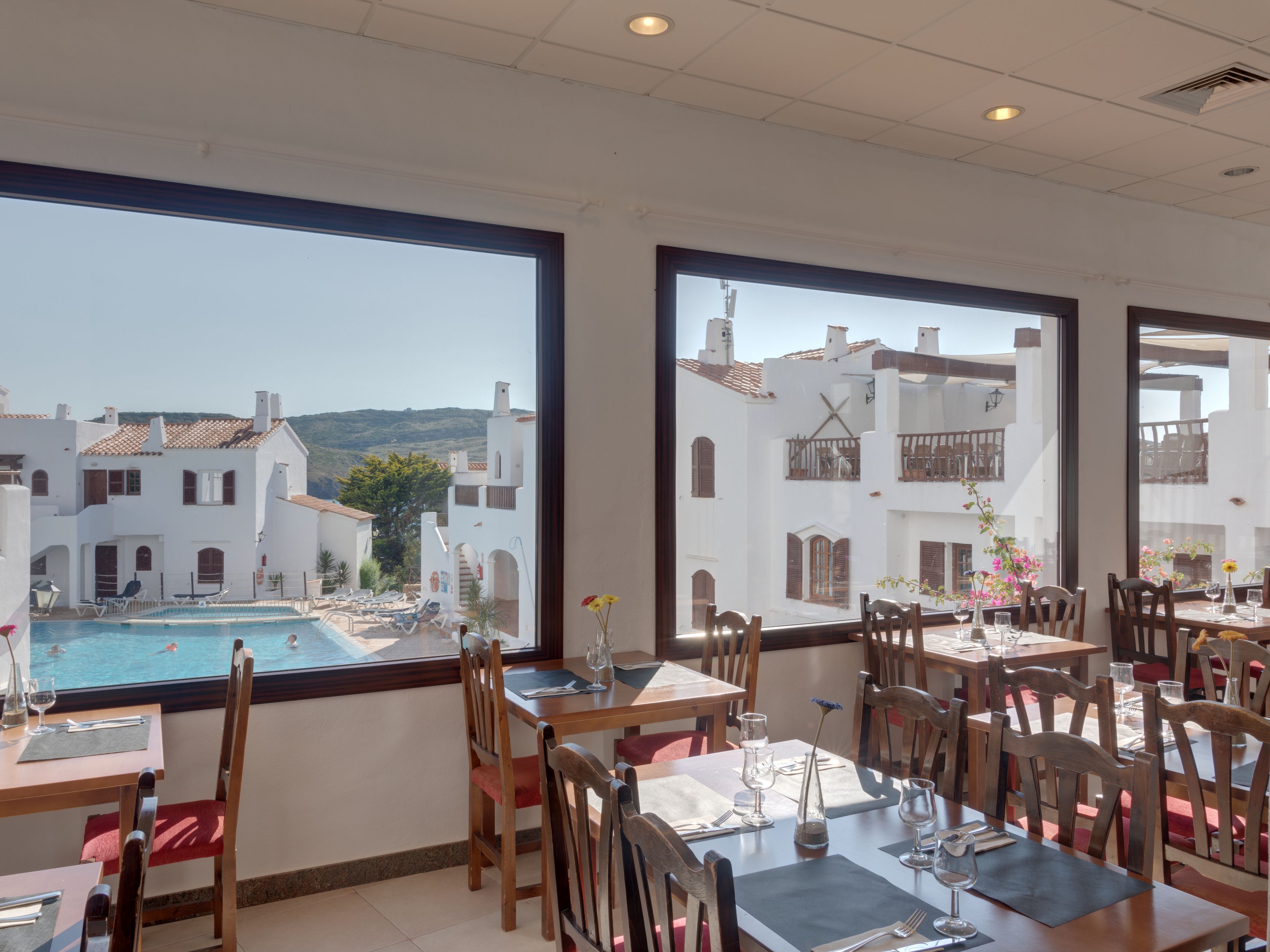Een restaurant met terras, met uitzicht op een zwembad en witte gebouwen met rode dakpannen.