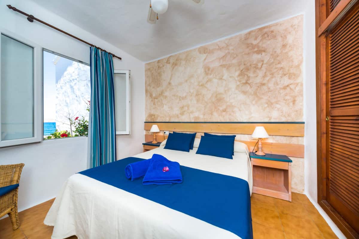Een hotelkamer met een bed, een raam met gordijnen, een nachtkastje en een houten deur.