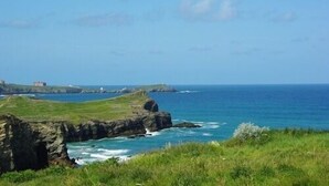 A coastal landscape with a rocky outcrop and a building in the distance. - Porth Lodge Hotel (Newquay)