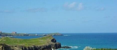 A coastal landscape with a rocky outcrop and a building in the distance.