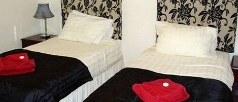 Two twin beds with matching headboards and pillows, a bedside table with a lamp, and a red towel on each bed.