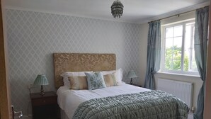 A bedroom with a large bed, a nightstand, a lamp, and a window with curtains. - Porth Lodge Hotel (Newquay)