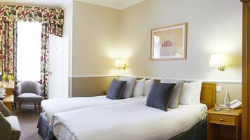 A hotel room with a large bed, two bedside tables, a chair, a desk, and a window with floral curtains.
