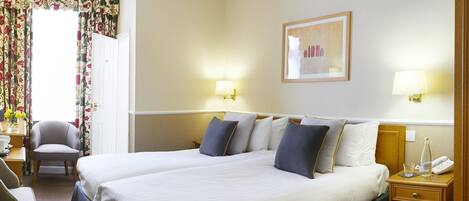 A hotel room with a large bed, two bedside tables, a chair, a desk, and a window with floral curtains.