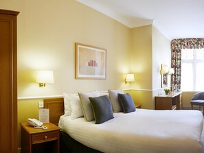 Habitación de hotel con una cama grande, dos lámparas de noche, un teléfono, un cuadro enmarcado en la pared y una ventana con cortinas.