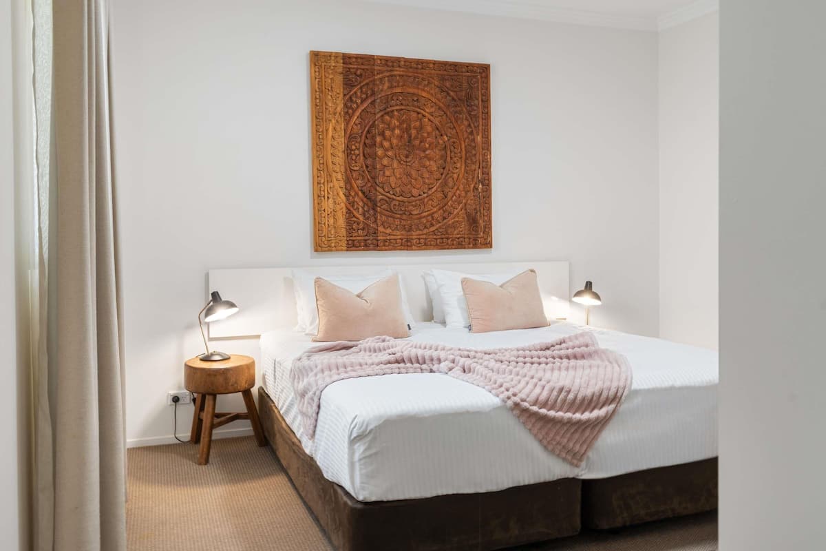 Une chambre à coucher avec un grand lit, deux tables de chevet, une œuvre d’art accrochée au mur et un sol recouvert d’une moquette.
