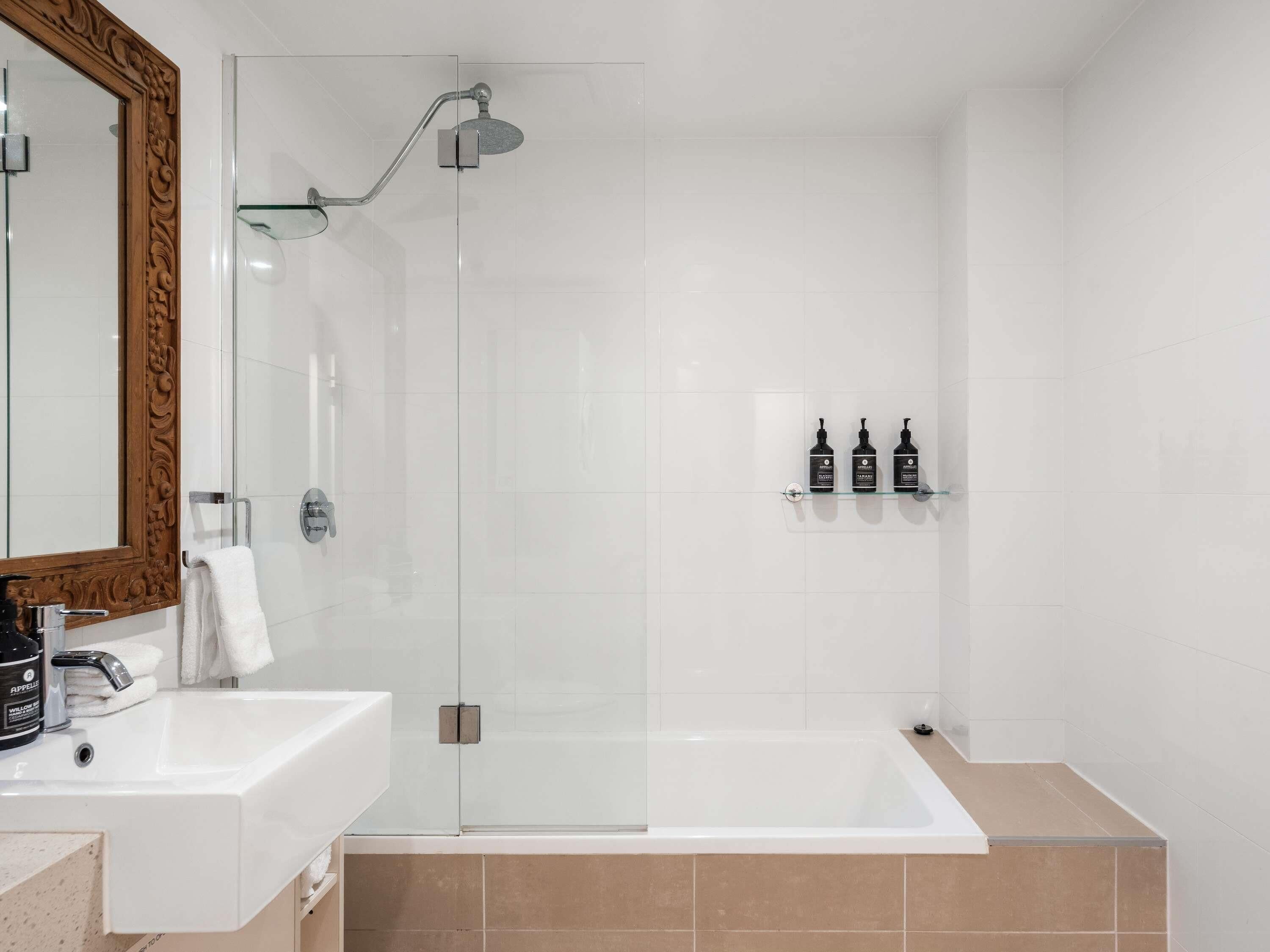 A modern bathroom with a glass shower enclosure, a white sink, a bathtub, and a mirror with an ornate frame.