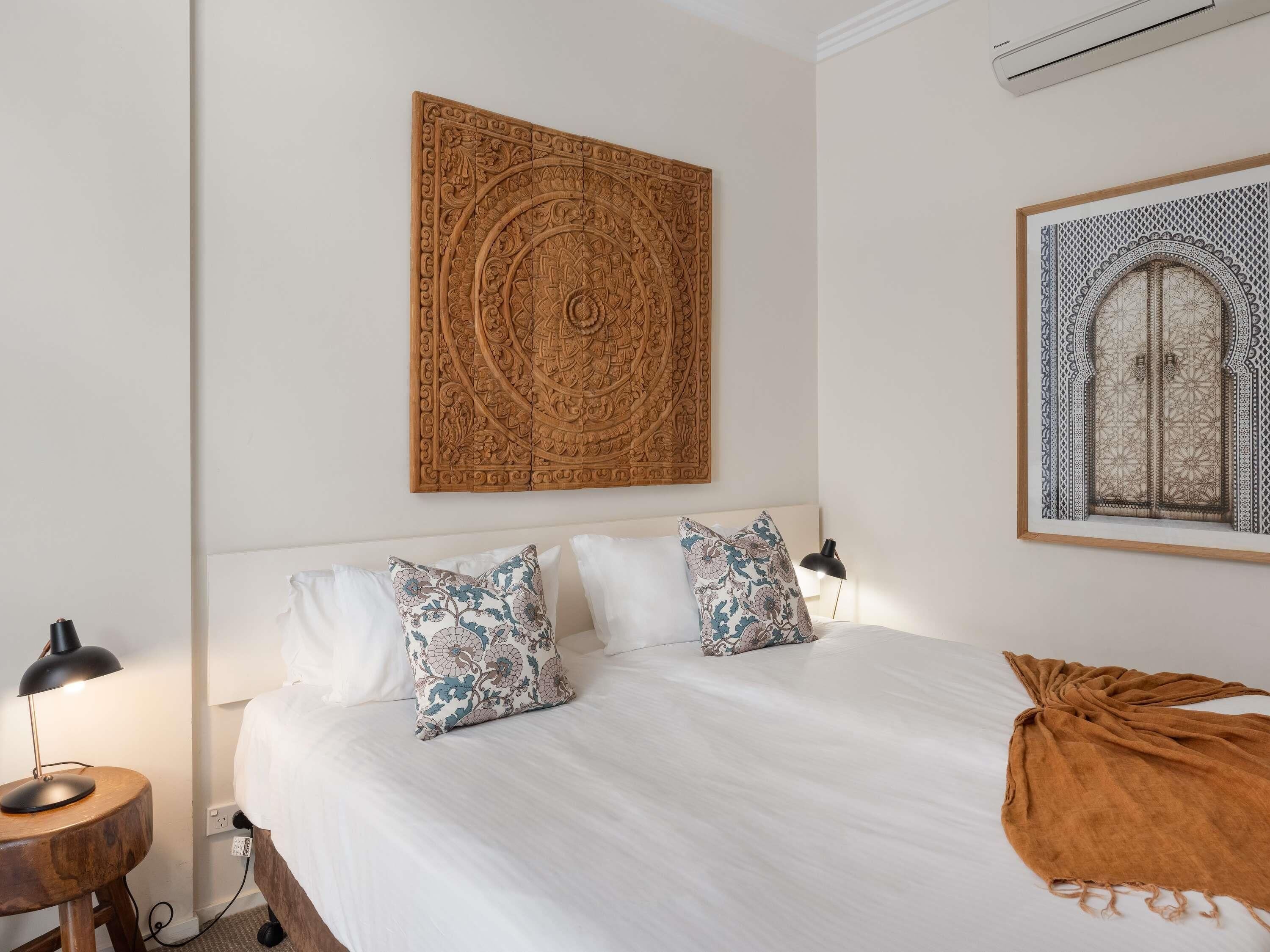 A bedroom with a bed, pillows, a nightstand, a lamp, and a wall-mounted artwork.